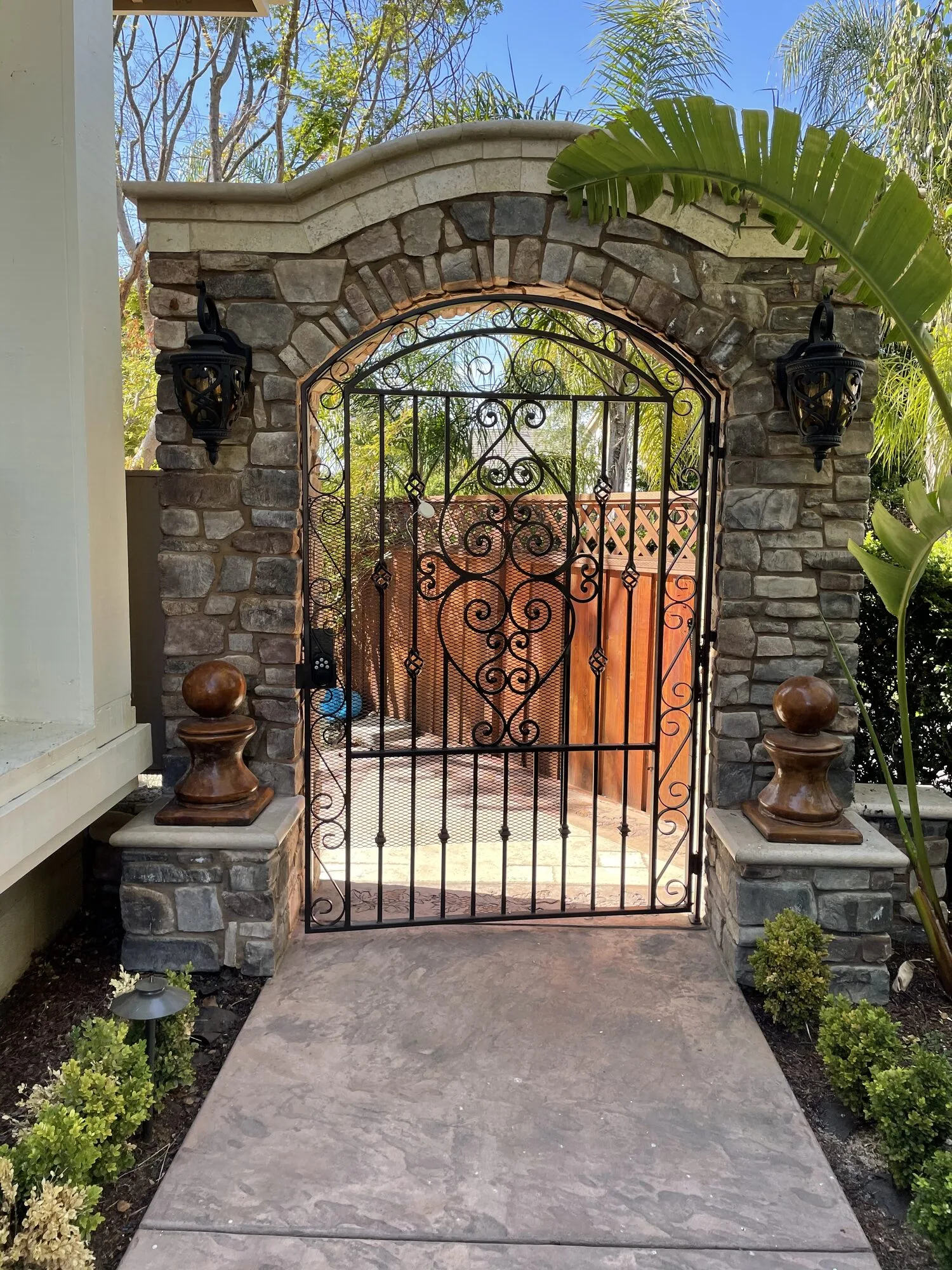 A stone entry arch and wrought-iron gate marking the garden arrival beside the house.