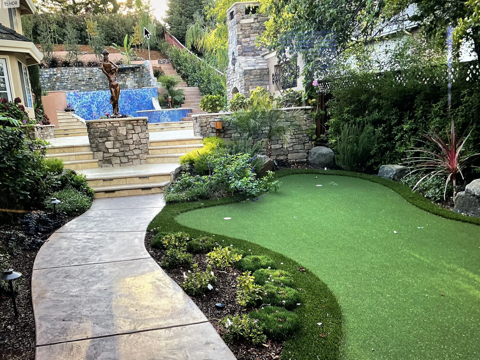 A curved putting green and garden path leading toward the pool and upper terraces.