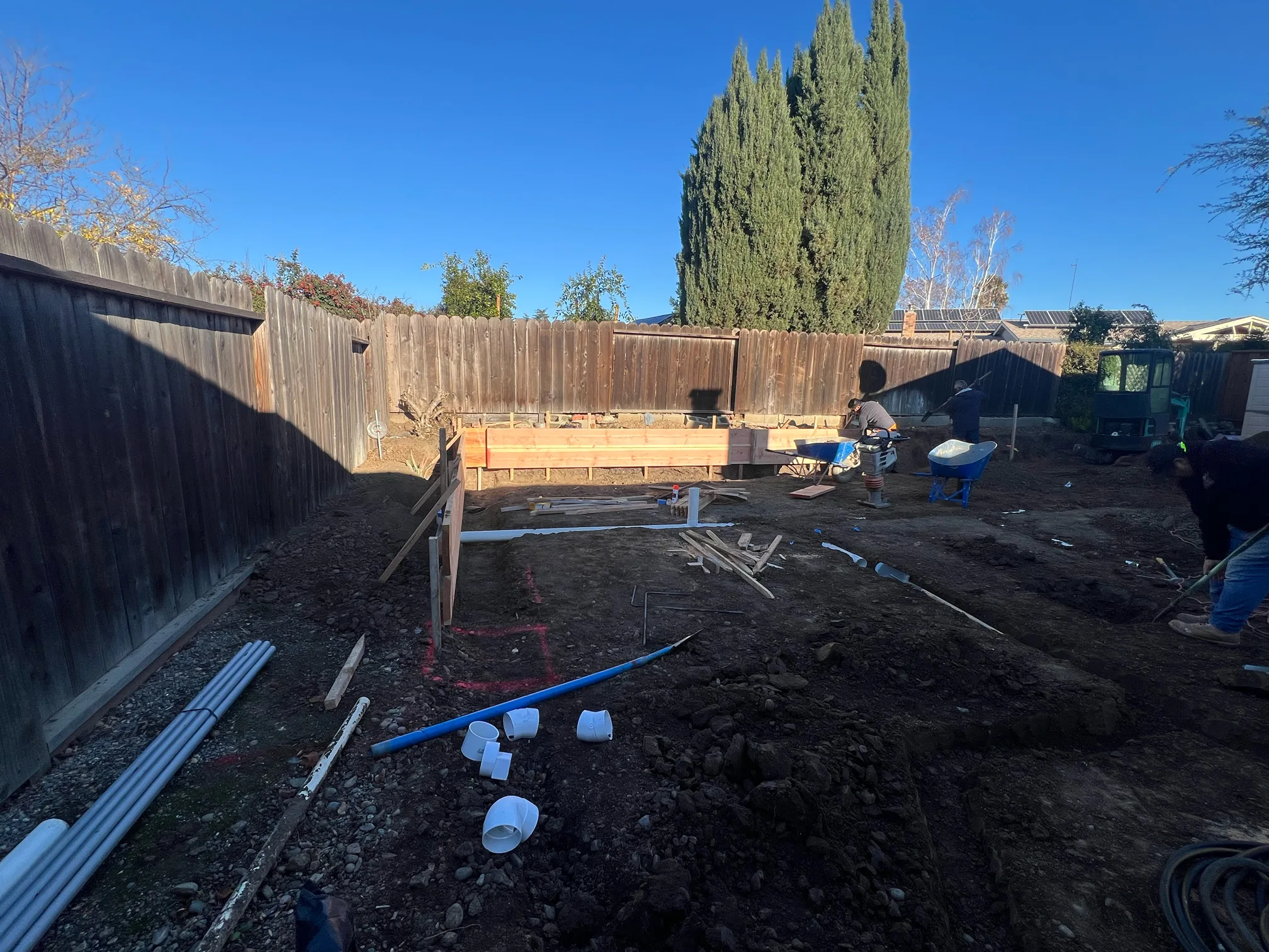 The cleared Hernandez backyard during drainage work, with utility pipes laid across excavated soil and concrete formwork under construction.