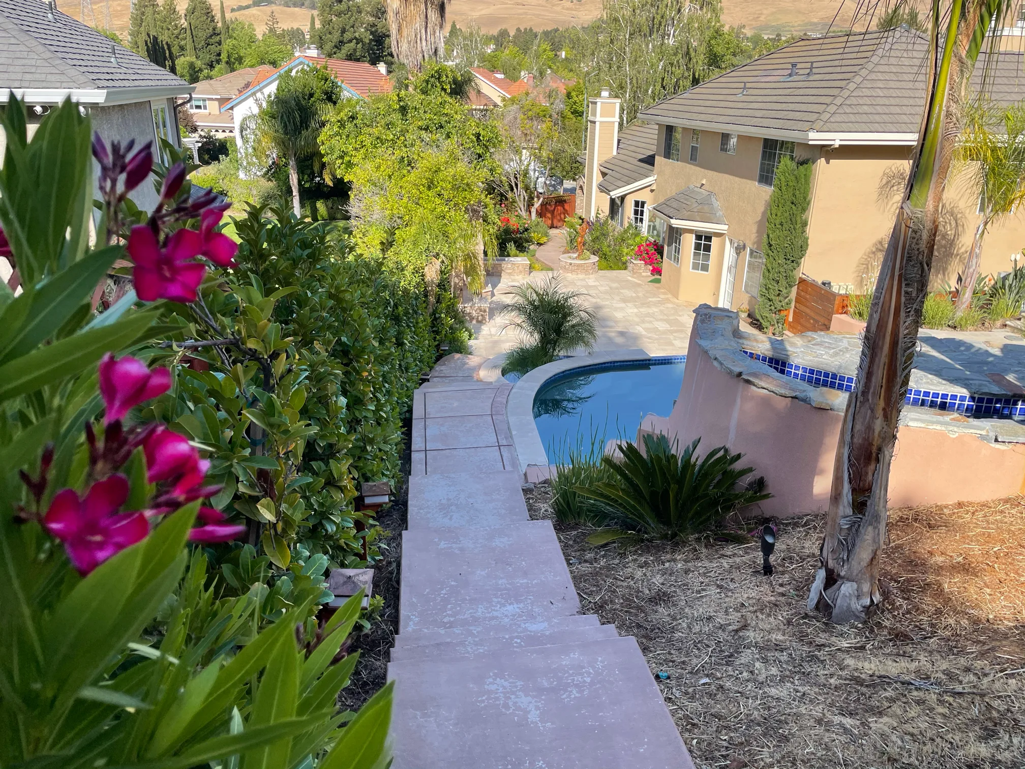 A planted hillside path descends beside the spa toward the lower courtyard and house.